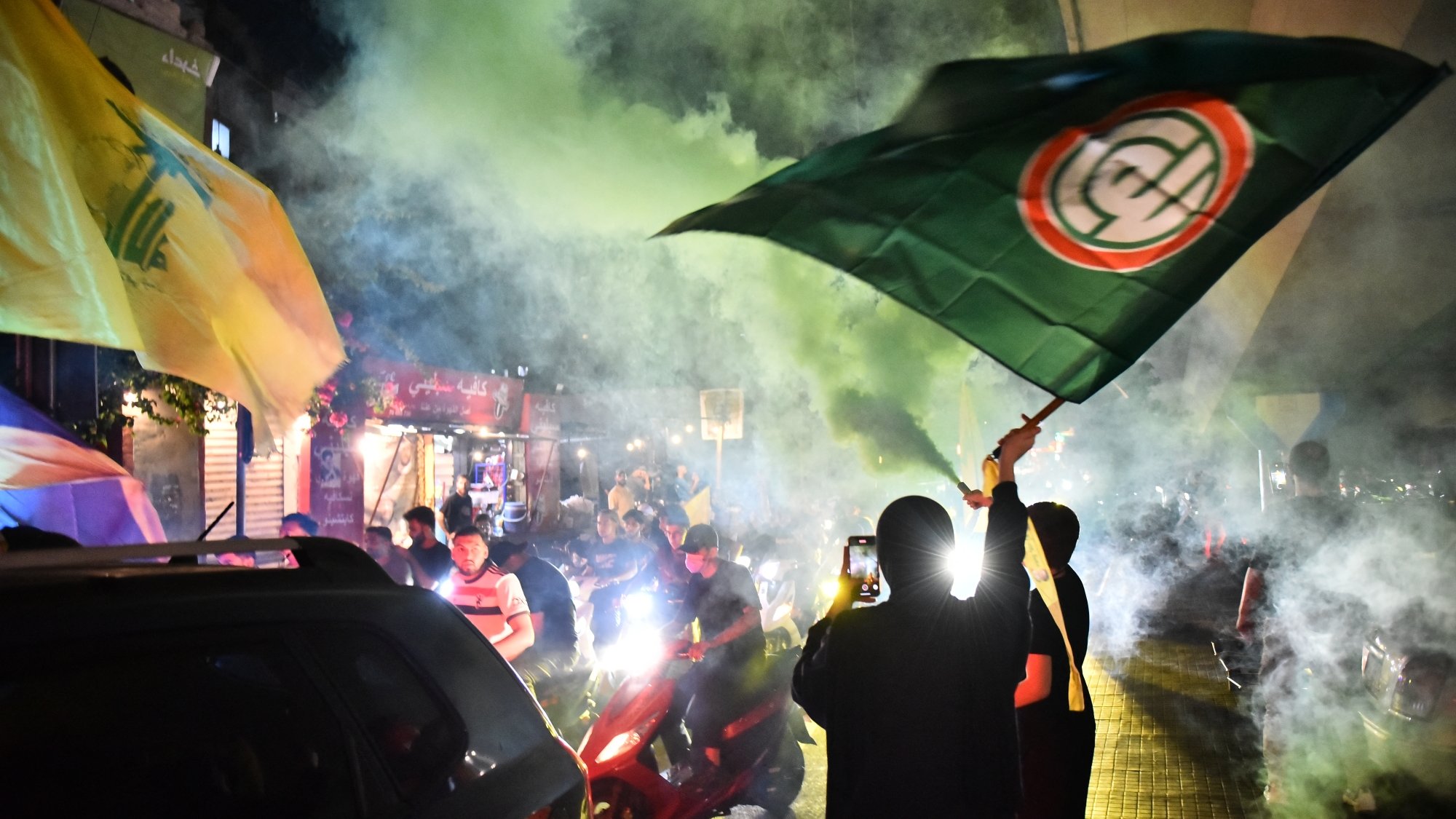 Des manifestants brandissent des drapeaux sous une fumée colorée dans une ambiance festive.