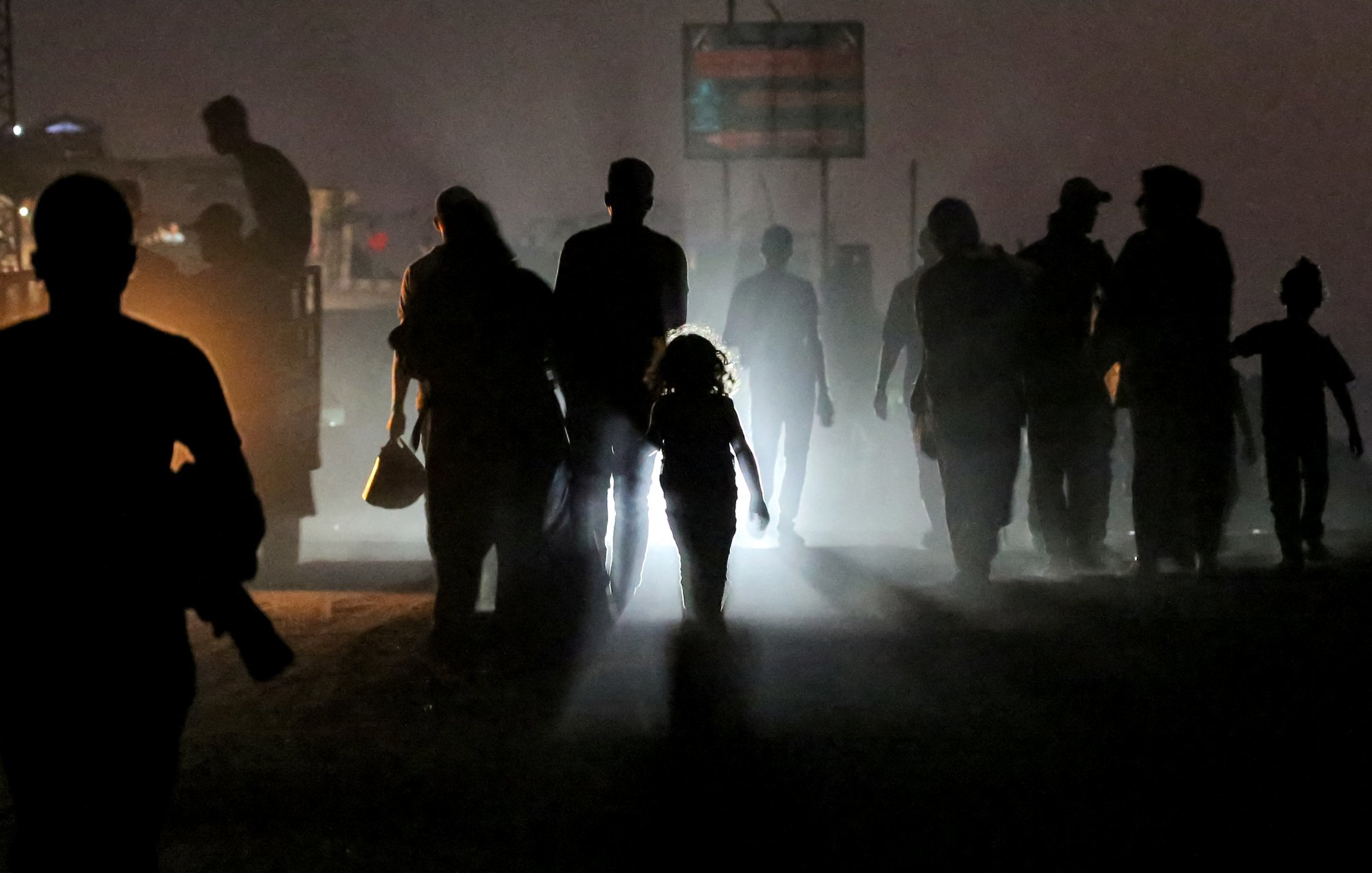 Silhouettes de personnes marchant dans une ambiance brumeuse, une enfant éclairée au centre.