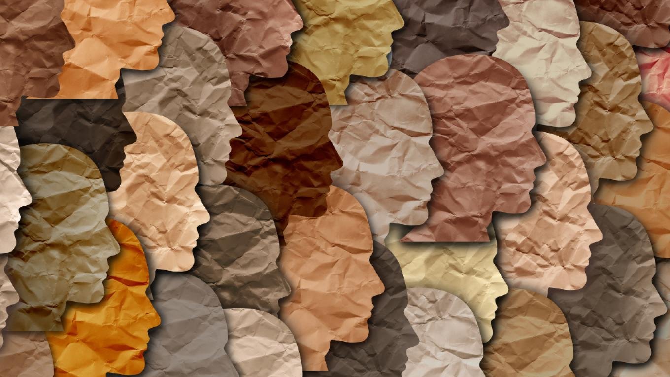 The image features a collage of human profiles created from various shades of crumpled paper. Each silhouette has a different tone, representing a diverse range of skin colors. The overlapping and varied textures of the paper give depth and interest to the composition, highlighting themes of diversity and inclusion. The overall effect is a harmonious blend of shapes and colors.