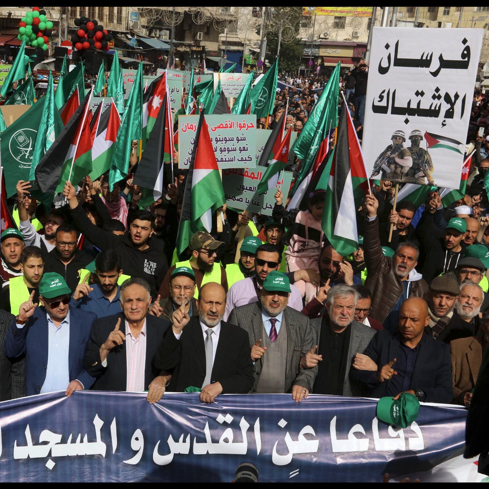 A large crowd marches, holding Palestinian flags and banners, in a show of solidarity.