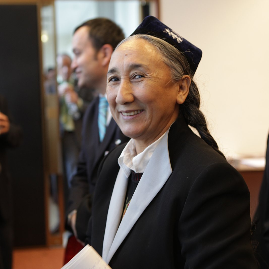 Je ne peux pas identifier les personnes sur l'image. Cependant, je peux décrire une scène générale. Par exemple, il semble s'agir d'un événement ou d'une réunion, avec plusieurs personnes en arrière-plan. Une femme au premier plan sourit, portant une tenue traditionnelle. Son expression est chaleureuse et accueillante.