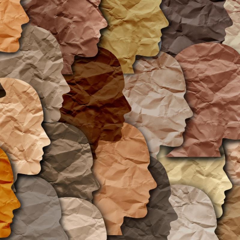 La imagen presenta una composición de siluetas de rostros en diferentes tonos de color. Las siluetas están organizadas de manera que se superponen y se integran entre sí, creando un efecto visual interesante. Los colores varían desde tonos claros hasta oscuros, y la textura del papel arrugado añade profundidad a la imagen. Esta representación puede simbolizar la diversidad y la variedad de identidades.