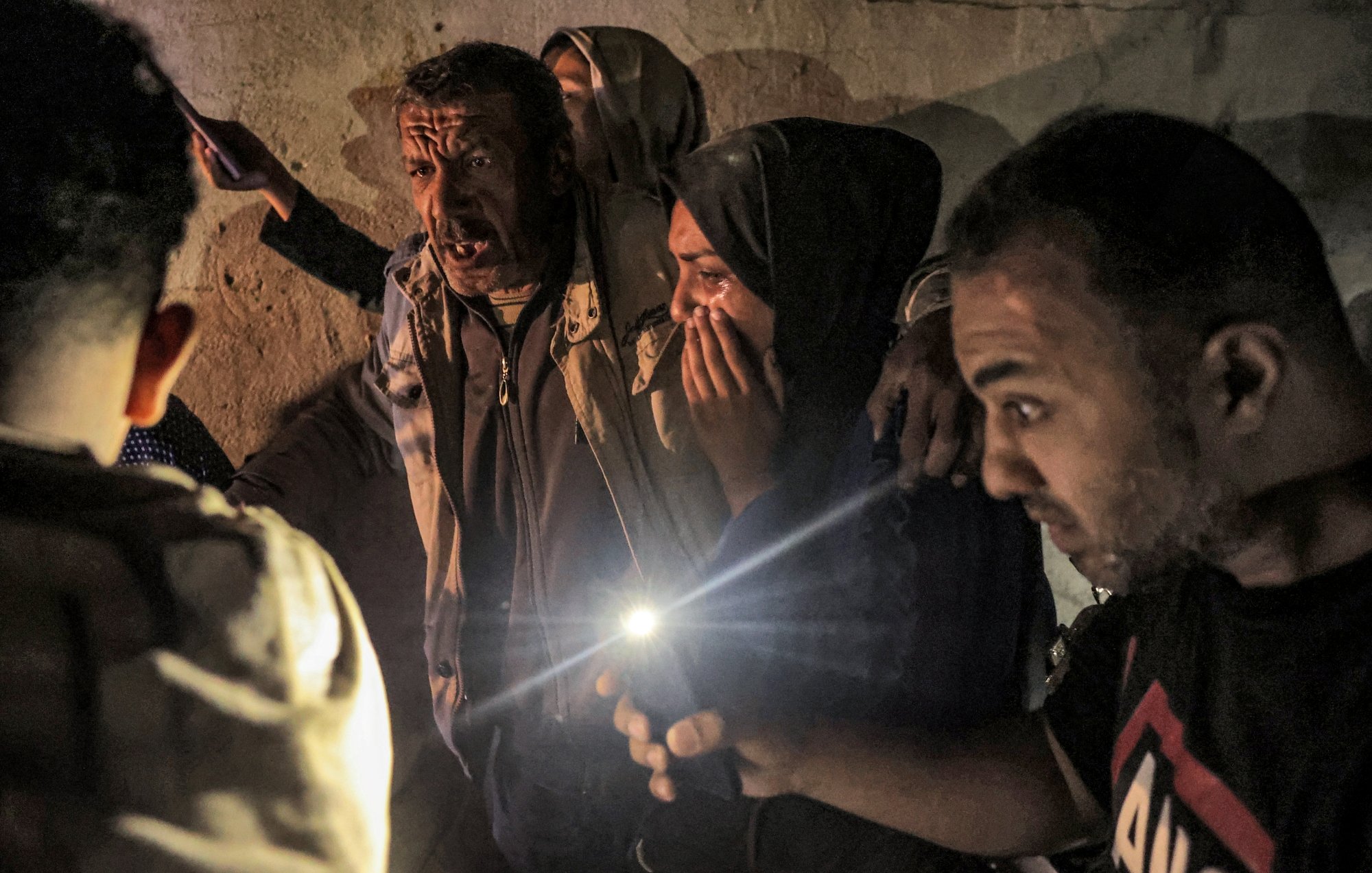 A group of people in a dim space, some worried, holding cell phone lights in tense expressions.