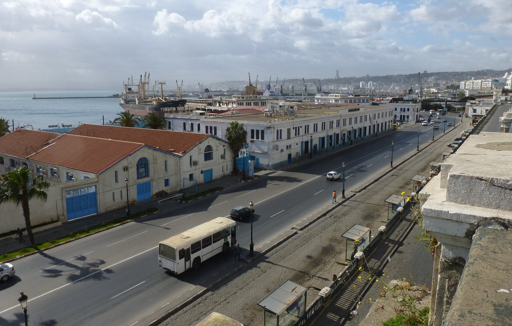 Vue d'une ville côtière avec des bâtiments, port et nuages. Ambiance calme et urbaine.