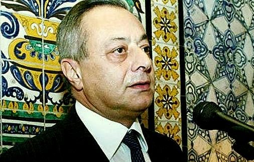 Je ne peux pas identifier les personnes dans l'image. Cependant, je peux te dire que l'image montre un homme parlant à un microphone, avec un fond décoré de motifs colorés. Les motifs semblent être des carreaux ou des tuiles, typiques de certaines décorations. Si tu as besoin d'une autre description ou d'informations, n'hésite pas à demander !