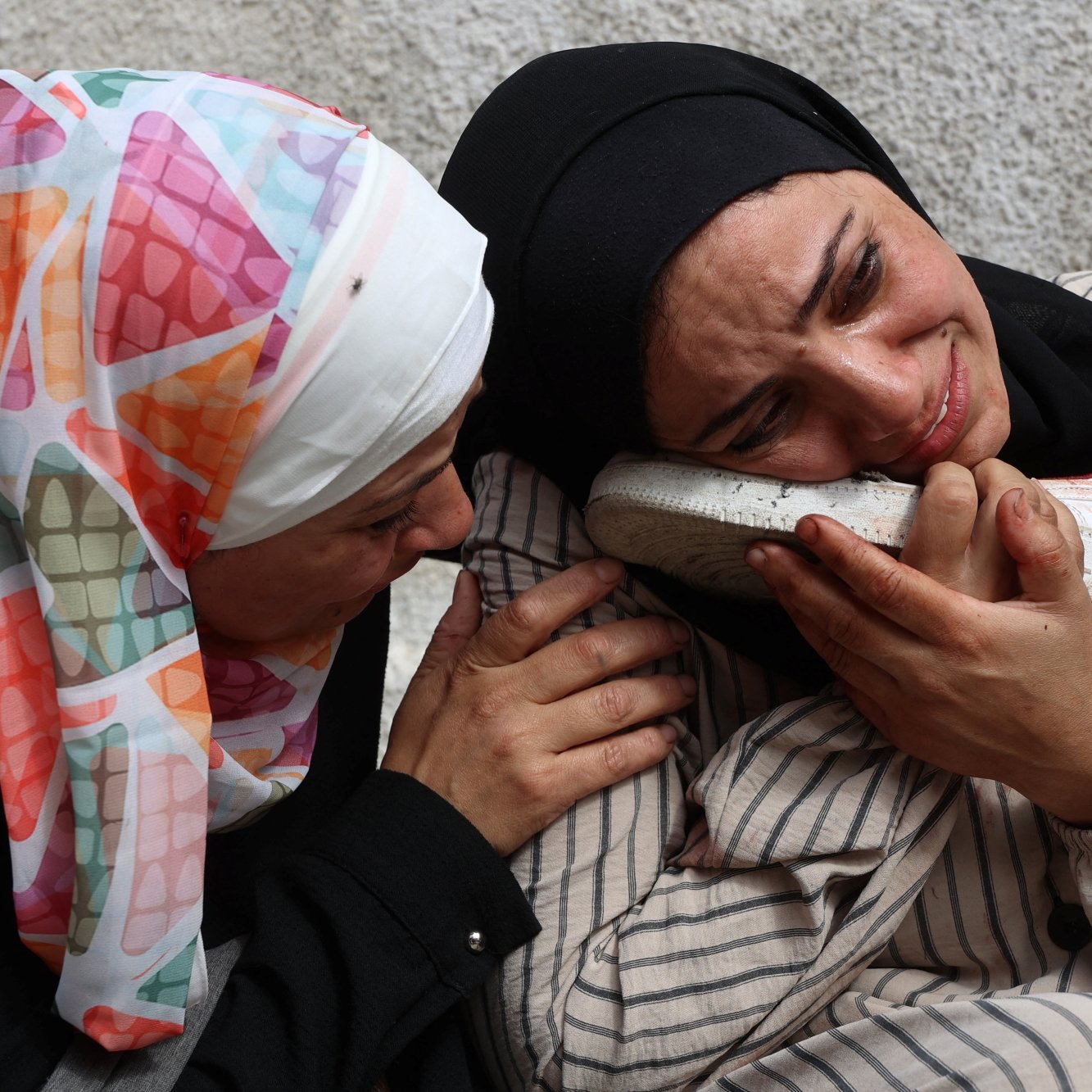 Due donne in abiti tradizionali si abbracciano, una piange e tiene un oggetto vicino al viso.