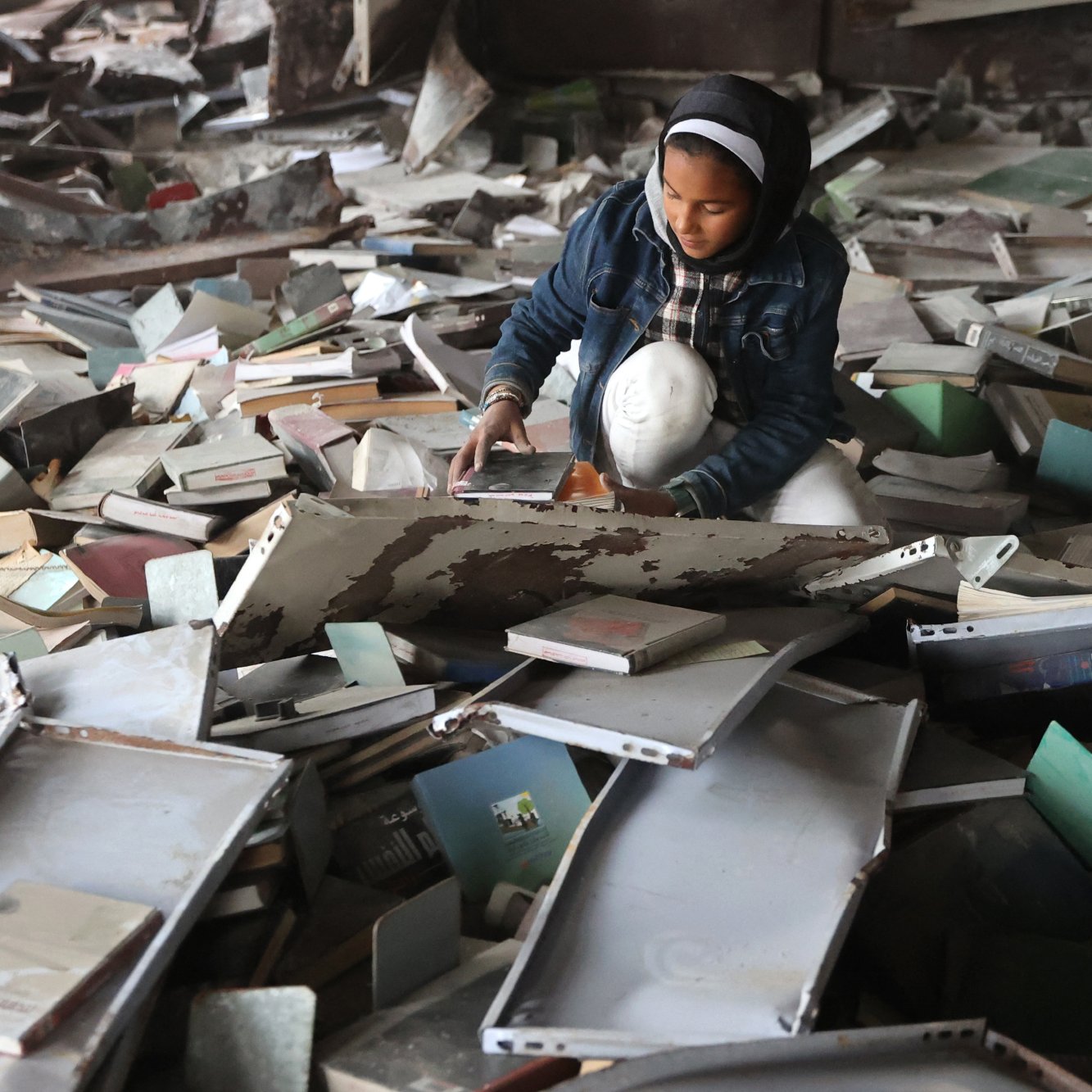 Una ragazza si trova in un luogo disordinato, circondata da libri e carte.