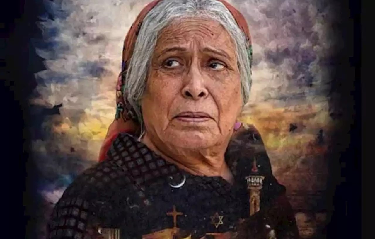 Cette image représente une femme âgée avec une expression pensive et préoccupée. Elle porte un foulard sur la tête et un vêtement sombre. En arrière-plan, on peut voir un paysage dramatique avec des nuages sombres et des silhouettes de bâtiments, évoquant peut-être un milieu rural ou historique. Le texte en bas de l'image semble être un titre ou un nom, mais il n'est pas identifiable sans plus de contexte. L'ensemble de la composition donne une impression d'émotion intense et de réflexion.