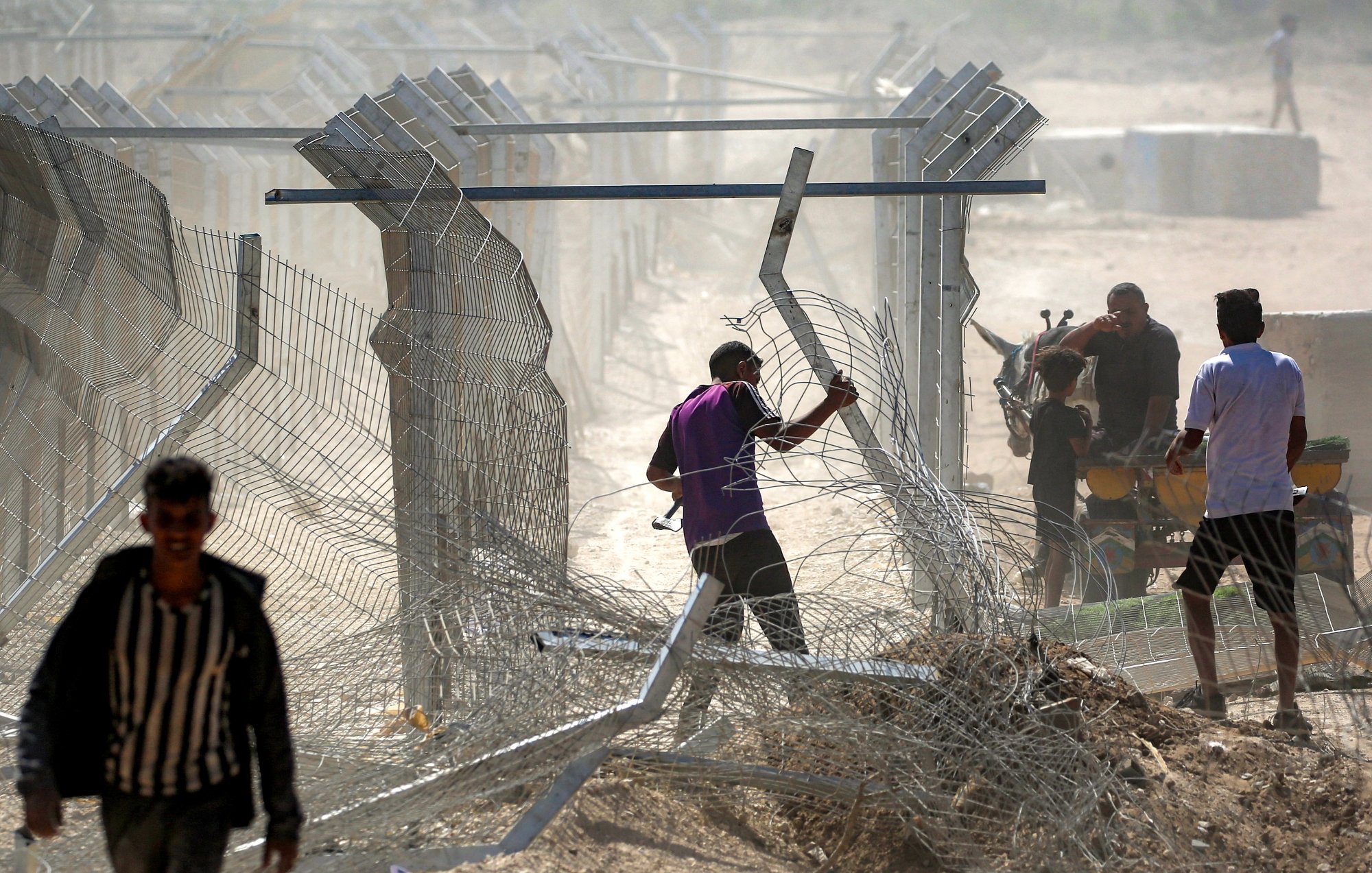 Des hommes manipulent des barbelés près d'une clôture dans un environnement poussiéreux.