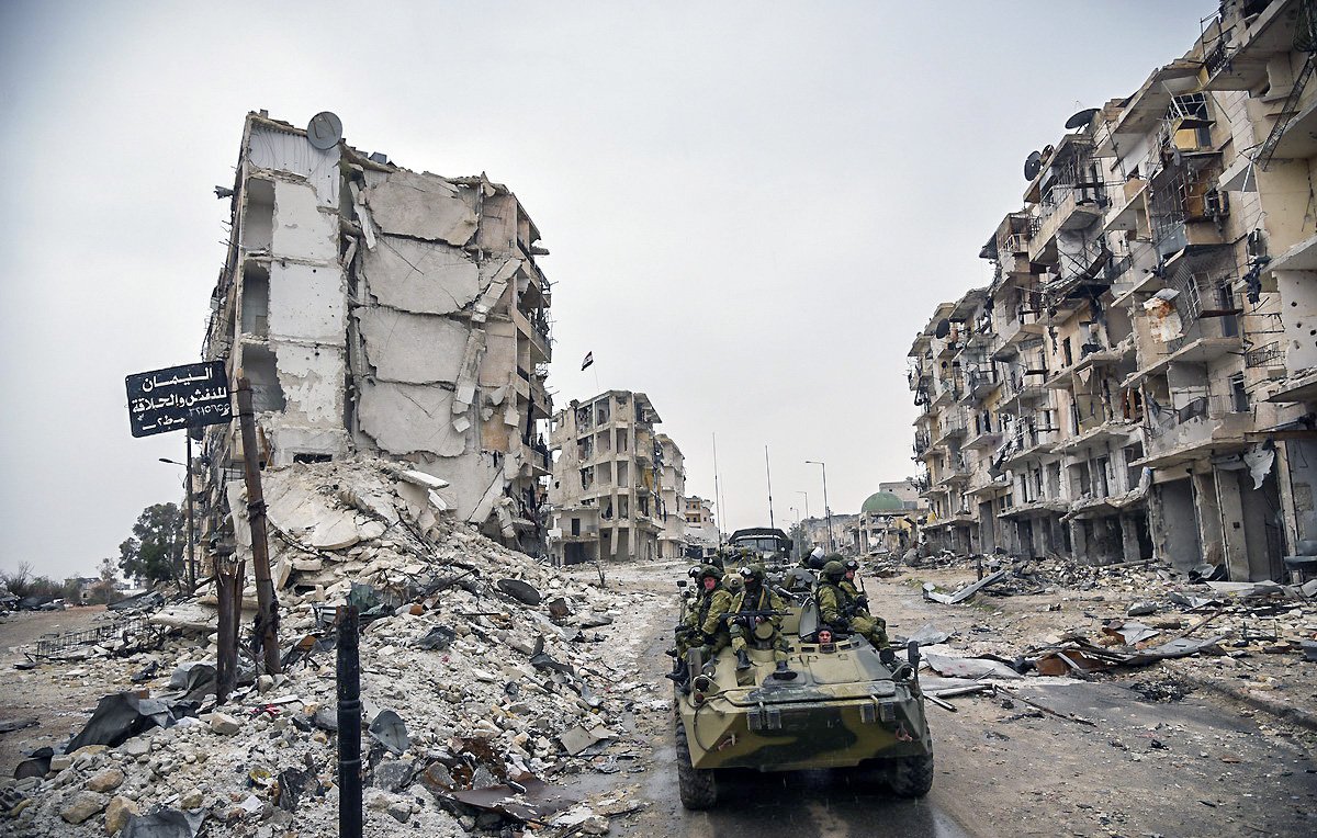 تصویر نشان‌دهندهٔ یک منطقهٔ ویران شده است که در آن چند ساختمان تخریب شده و در حال فرو ریختن به نظر می‌رسند. در این صحنه، یک وسیله نقلیه نظامی در حال حرکت است و تعدادی سرباز در آن نشسته‌اند. بقیهٔ محیط شامل زباله‌ها و نشانه‌های ویرانی است که به وضعیت بحرانی منطقه اشاره دارد. هوا ابری و تیره به نظر می‌رسد و فضایی خالی و ساکت را ایجاد کرده است.