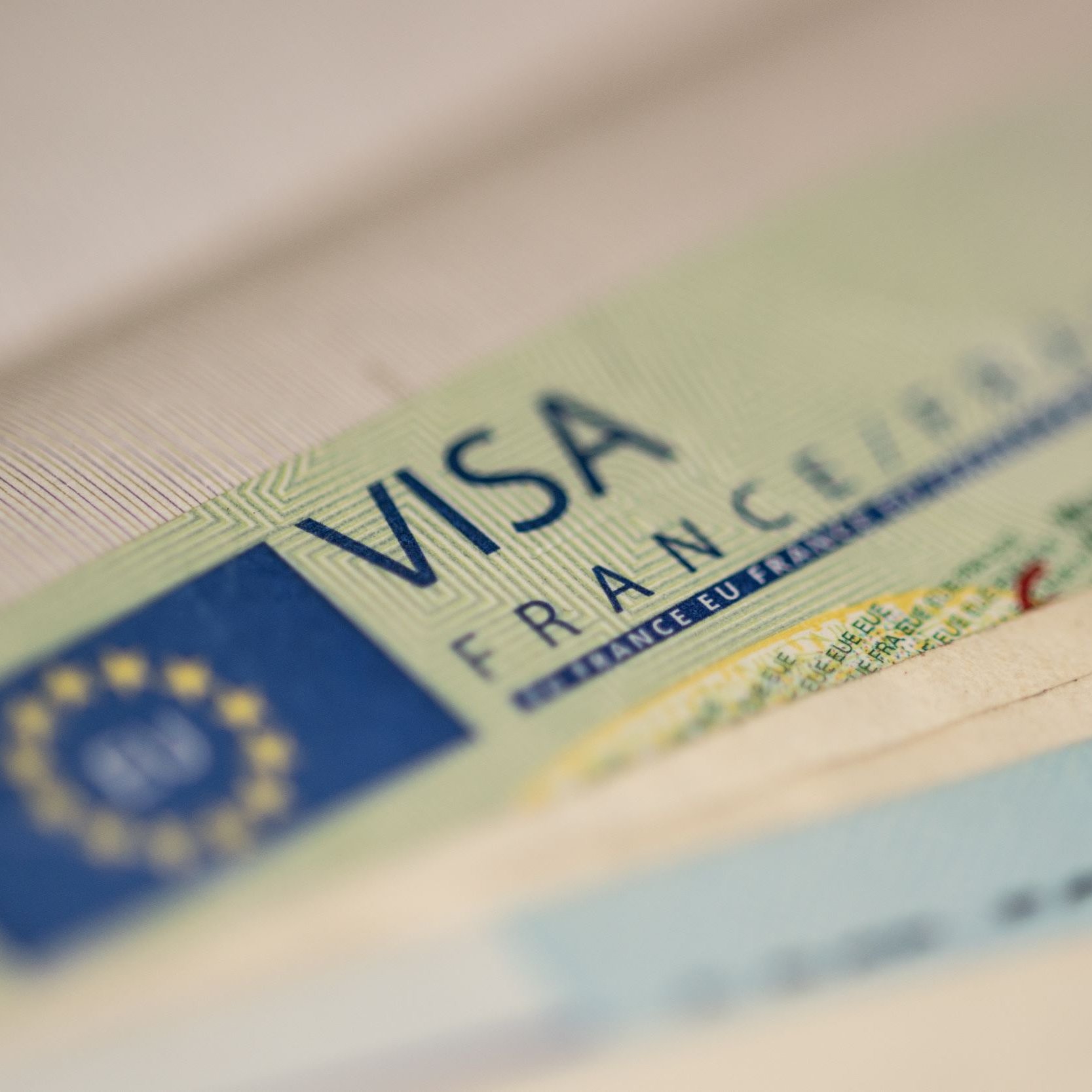 L'image montre un document de type visa, probablement un visa français. On peut voir le mot "VISA" en lettres majuscules, ainsi que des détails graphiques et textuels associés, comme le terme "FRANCE". En arrière-plan, on aperçoit des billets de banque, ce qui suggère un contexte lié à des voyages ou à des transactions. L'ensemble est présenté de manière à mettre l'accent sur le visa.