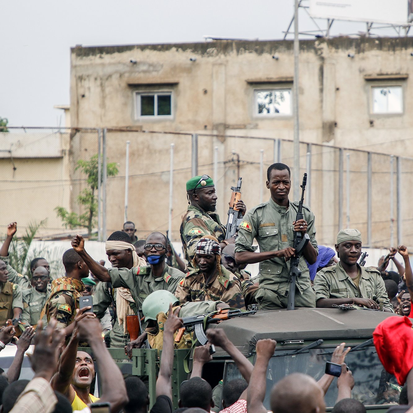 در این تصویر، تعدادی نظامی با لباس نظامی و سلاح در دست در بالای یک خودروی نظامی ایستاده‌اند. اطراف آن‌ها جمعیتی از مردم دیده می‌شود که در حال خوشحالی و حمایت از نظامی‌ها هستند و دست‌هایشان را بالا برده‌اند.背景 تصویر نیز ساختمان‌هایی دیده می‌شود که نشان از یک فضای شهری دارد. احساس این تصویر نشان‌دهنده شور و هیجان جمعیت به خاطر نظامی‌ها است.