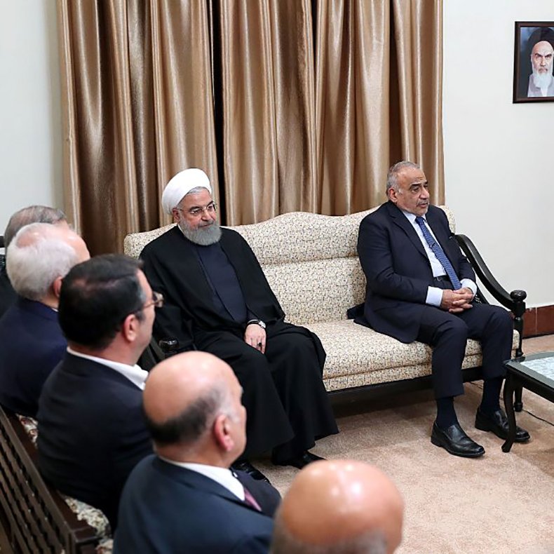 در این تصویر، چند نفر در یک اتاق رسمی نشسته‌اند. شخصی در سمت راست تصویر با لباس مشکی و عمامه، رهبر جمهوری اسلامی ایران است. در مجاورت او، فرد دیگری نشسته که به نظر می‌رسد مرتبط با مقامات دولتی باشد. در سمت چپ، افراد دیگری در حال گوش دادن به صحبت‌ها هستند. دیوارها با پرده‌های قهوه‌ای تزیین شده و پرچم جمهوری اسلامی ایران در پس‌زمینه دیده می‌شود. یک تصویر از بنیان‌گذار جمهوری اسلامی نیز بر دیوار نصب شده است. جو تصویر رسمی و جدی به نظر می‌رسد.