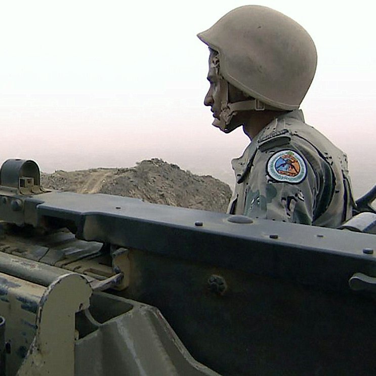 تظهر في الصورة جندي يرتدي خوذة وقميص عسكري، وهو يقف بجانب مدفع ثقيل ينظر نحو منطقة بعيدة. تكتنف الصورة أجواء ضبابية، مما يعطي انطباعًا بوجود حالة من الترقب أو الحذر. هذه الصورة تعكس صورة للوحدة العسكرية والتركيز في مهمة معينة.