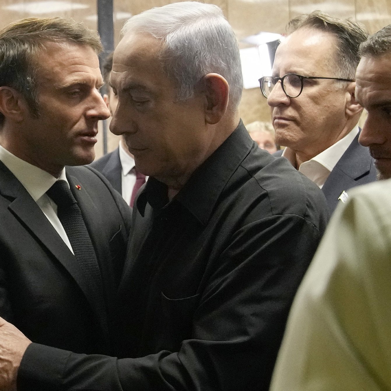 این تصویر به یک موقعیت نزدیک و تعاملی بین دو نفر اشاره دارد. یک نفر در لباس رسمی تیره و دیگری نیز به شکلی مشابه پوشیده است. به نظر می‌رسد که آن‌ها در حال گفت‌وگو یا تبادل نظر هستند و احساس نزدیکی را به نمایش می‌گذارند. در پس‌زمینه، چند نفر دیگر نیز قرار دارند که توجه‌شان به این دو نفر جلب شده است. فضای تصویر حالت جدی و مهمی دارد.