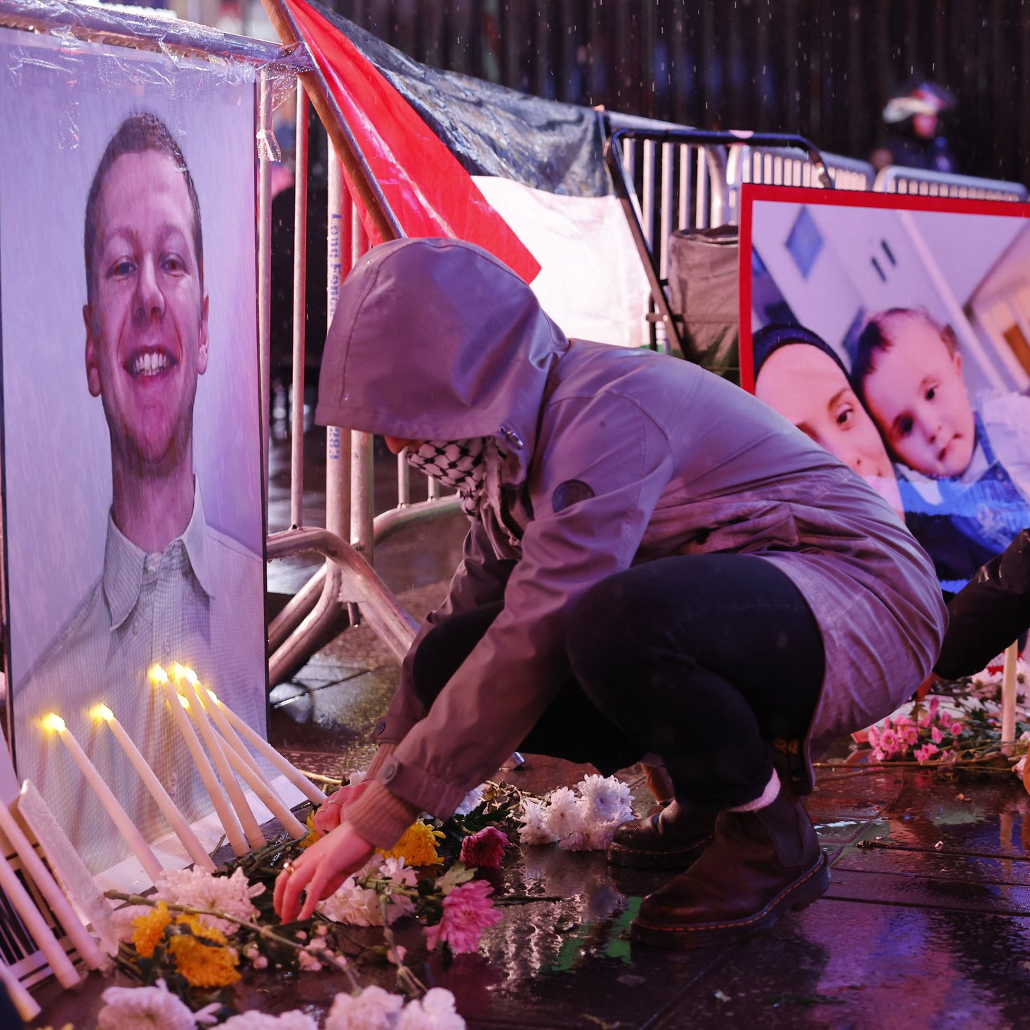 تصویر فضای یک تجمع یادبود را نشان می‌دهد که در آن افراد در حال قرار دادن شمع و گل هستند. در جلوی آنها، تصاویری از یک فرد و یک خانواده به نمایش گذاشته شده است. باران به زمین می‌ریزد و خیابان براق است. افراد با لباس‌های گرم و کلاه روی زمین نشسته‌اند و به یاد افرادی که از دست رفته‌اند، مراسمی برگزار می‌کنند. این صحنه حال و هوای غم و اندوه را منتقل می‌کند.