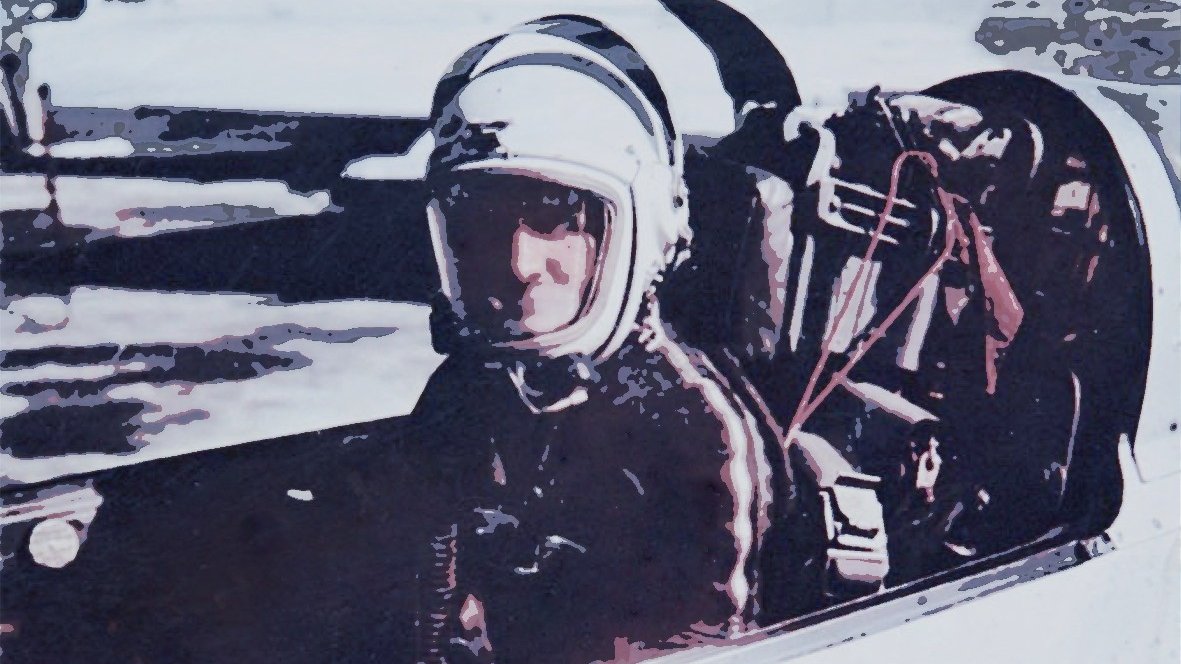 L'image montre un pilote assis dans le cockpit d'un avion ou d'un vaisseau spatial. Il porte un casque de protection et une combinaison, ce qui indique qu'il est probablement en préparation pour un vol. Le décor autour de lui semble être un environnement aéroporté ou une piste de lancement. L'ambiance de l'image évoque la technologie et l'exploration aérienne ou spatiale.