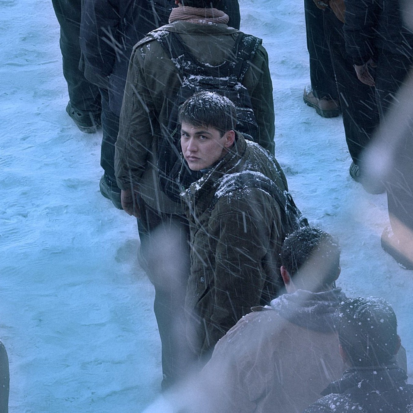 تصویر گروهی از افراد در برف است. یک جوان در مرکز با نگرانی به دور نگاه می‌کند. برف باریده و فضایی سرد است.