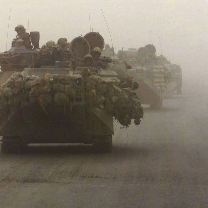 در تصویر، چندین تانک در حالی که در مه و گرد و غبار حرکت می‌کنند، به نمایش درآمده‌اند. تانک‌ها به طرز مشخصی بارگذاری شده‌اند و تجهیزات نظامی بر روی آن‌ها دیده می‌شود. محیط اطراف به شدت مه‌آلود است و دید محدود است. فضای تصویر حس تنش و حرکت در یک منطقه نظامی را منتقل می‌کند.