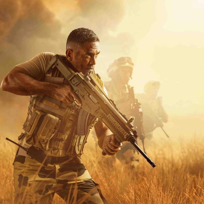 تظهر الصورة مشهدًا عسكريًا في بيئة صحراوية أو مفتوحة. يُرى في المقدمة رجل يرتدي زيًا عسكريًا ويحمل سلاحًا، يبدو مركزًا وجادًا. في الخلفية، يظهر عدد من الجنود الآخرين يتقدمون معه، مما يعزز الإحساس بالتعاون والعمل الجماعي. السماء تمتزج بألوان دافئة، مما يضيف جوًا من التوتر والحركة.