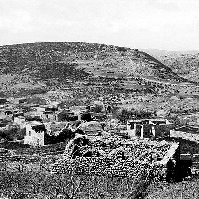 این تصویر نمایی از یک منطقه روستایی را نشان می‌دهد. در این تصویر، ویرانه‌های سازه‌های سنگی و خانه‌های قدیمی دیده می‌شوند که در میان تپه‌ها و زمین‌های زراعی قرار دارند. پوشش گیاهی محدود است و تپه‌ها با خاک و سنگ پوشیده شده‌اند. آسمان نیز به طور کلی ابری به نظر می‌رسد، که به فضای تصویر حالتی خاص می‌بخشد. این صحنه به نوعی حس تاریخ و قدمت را منتقل می‌کند.