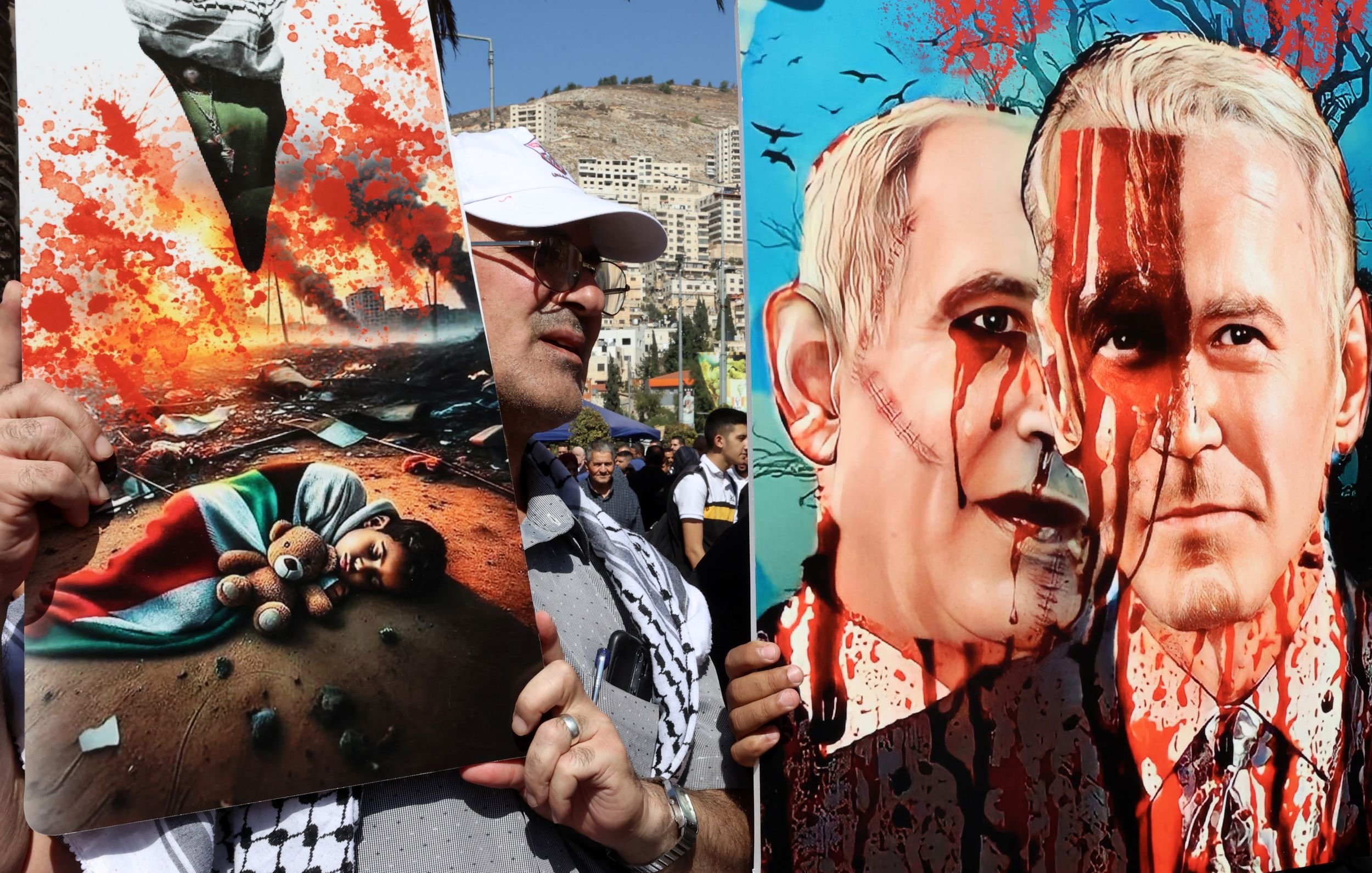 L'image montre des manifestants tenant des pancartes lors d'une démonstration. À gauche, une affiche illustre une scène tragique avec un enfant couché sur le sol, entouré de débris et d'une atmosphère de destruction. À droite, une illustration satirique ou critique représente deux figures, avec des visages peints évoquant des thèmes de violence, symbolisés par des éclaboussures de sang. L'ensemble évoque des questions politiques et humanitaires, avec un fort impact visuel.