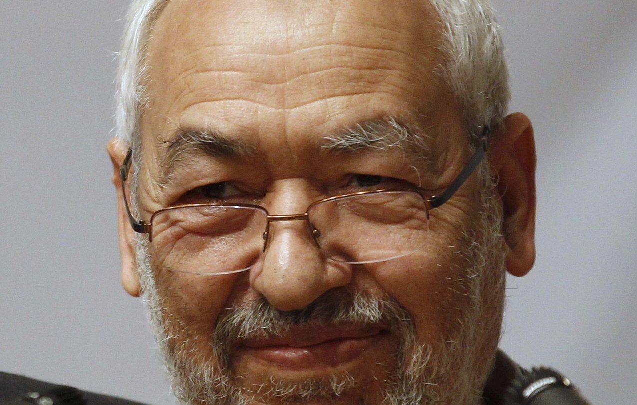 Je ne sais pas qui est cette personne, mais je peux décrire l'image de manière générale. Il s'agit d'un homme d'âge mûr avec des cheveux grisonnants et une barbe. Il porte des lunettes et a un sourire serein. L'arrière-plan semble être flou, ce qui attire l'attention sur lui. Les microphones à proximité suggèrent qu'il pourrait être en train de parler lors d'un événement ou d'une conférence.