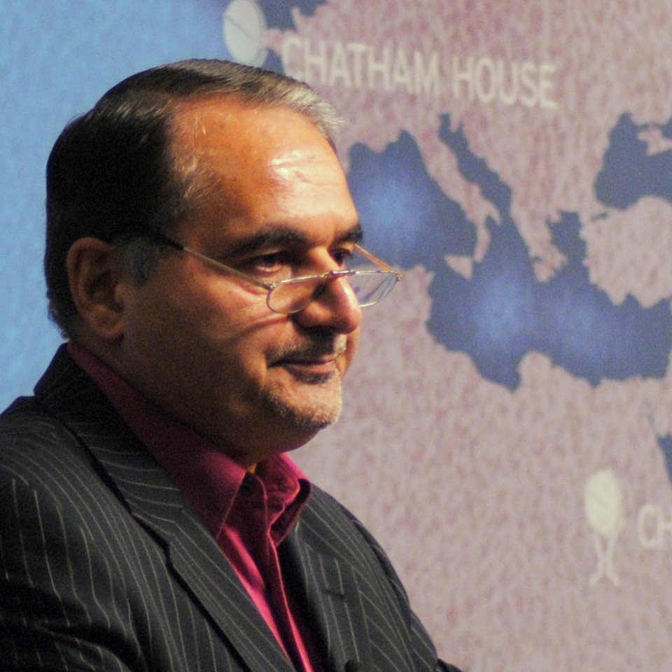 Je ne peux pas identifier qui est dans l'image, mais je peux te dire que c'est une photo d'un homme en costume, portant des lunettes, qui semble s'adresser à un public. En arrière-plan, il y a une carte du Moyen-Orient avec des indications de l'institution "Chatham House". L'ambiance suggère qu'il s'agit d'une conférence ou d'une présentation.