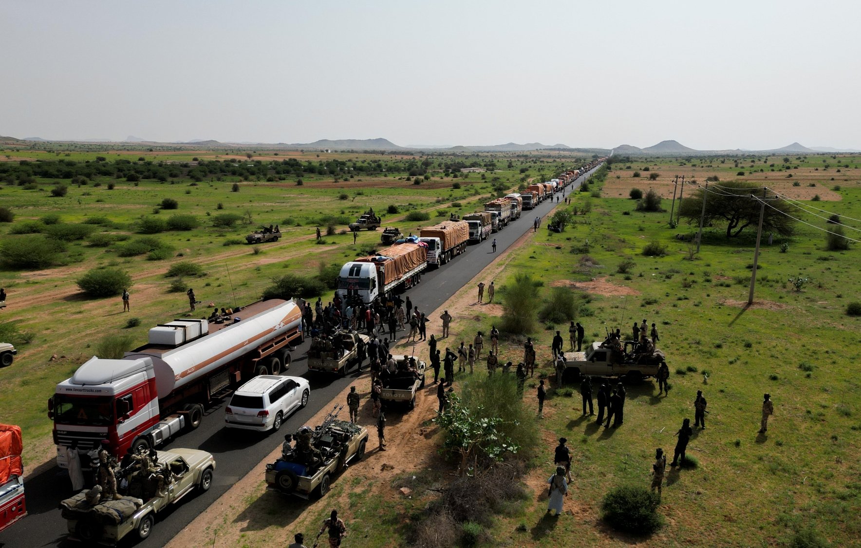 Una lunga fila di veicoli su una strada in un paesaggio verde e desertico.