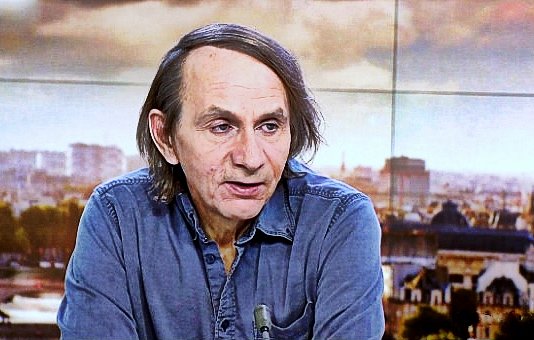 Je ne peux pas identifier les personnes dans l'image. Cependant, je peux vous aider à décrire une scène ou un contexte. Par exemple, si l'image montre une personne à la télévision, vous pourriez dire qu'elle est en discussion ou en interview, avec un arrière-plan urbain. Si vous avez des éléments spécifiques en tête, n'hésitez pas à les partager !