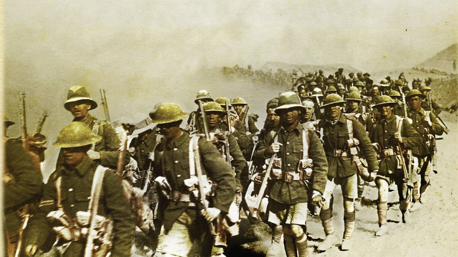 L'image représente un groupe de soldats en marche, probablement pendant une période de conflit. Ils portent des uniformes militaires, y compris des casques et des équipements de combat. Les soldats avancent sur un terrain poussiéreux, et il semble qu'ils soient dans un environnement difficile, avec une atmosphère chargée de fumée ou de poussière. L'image donne une impression de détermination et de camaraderie parmi les troupes.
