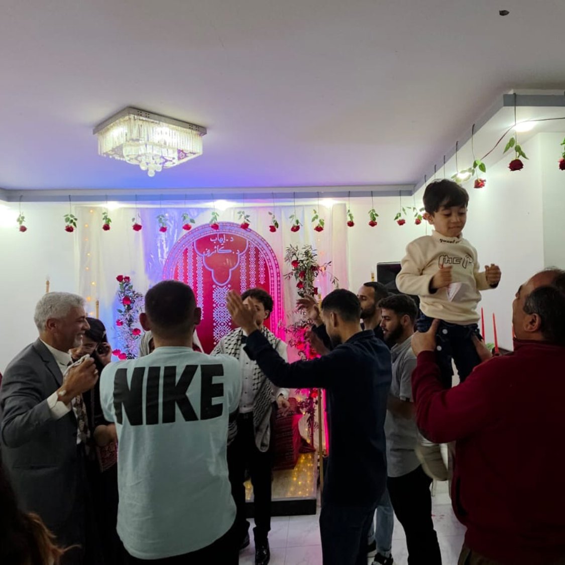 Una festa con persone che ballano, decorazioni floreali e un bambino in braccio.