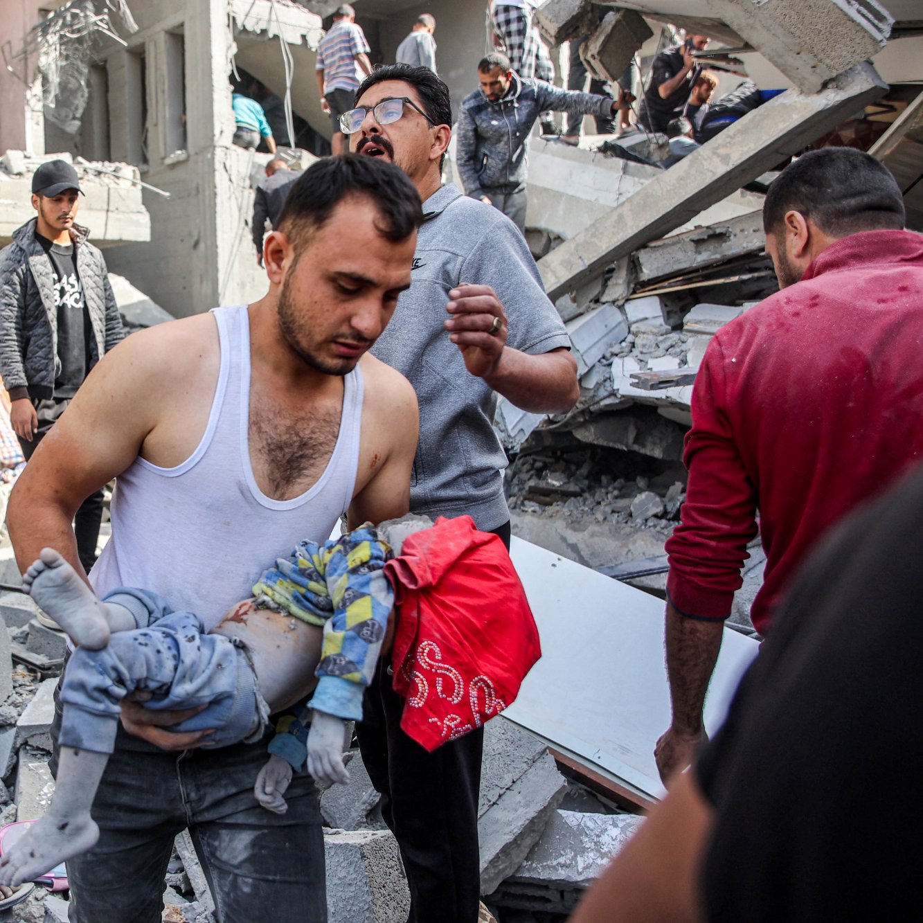 این تصویر صحنه‌ای از یک واقعه مشهود را نشان می‌دهد که در آن افراد در حال کمک به یکدیگر هستند. یک مرد در حال حمل یک کودک است که به نظر می‌رسد دچار آسیب شده است. در پس‌زمینه، خرابی‌های قابل توجهی از ساختمان‌های تخریب‌شده و نمایانگر شرایط دشوار موجود در این صحنه هستند. افراد دیگری نیز در تصویر دیده می‌شوند که در حال تلاش برای کمک به آسیب‌دیدگان هستند. احساس اضطراب و نگرانی در چهره‌ها و حرکات افراد محسوس است.