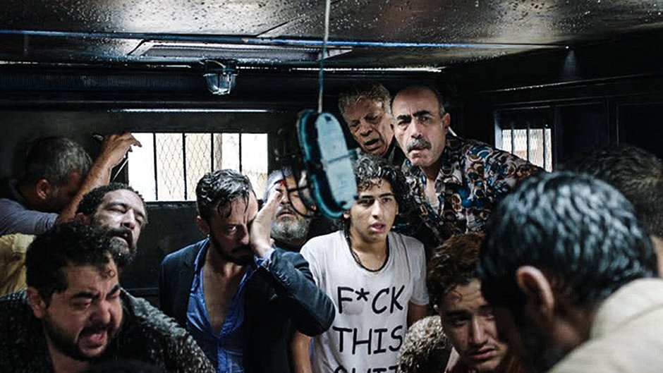 الصورة تظهر مجموعة من الأشخاص الذين يتواجدون في مكان مغلق، يبدو عليهم الارتباك والقلق. هناك مظاهر للفوضى، حيث يظهر بعضهم بمظهر متعب أو مضغوط. الإضاءة في المكان ضعيفة، مما يضيف شعورًا بالتوتر. يبدو أن الوضع في الصورة يعكس حالة صعبة أو حرجة.