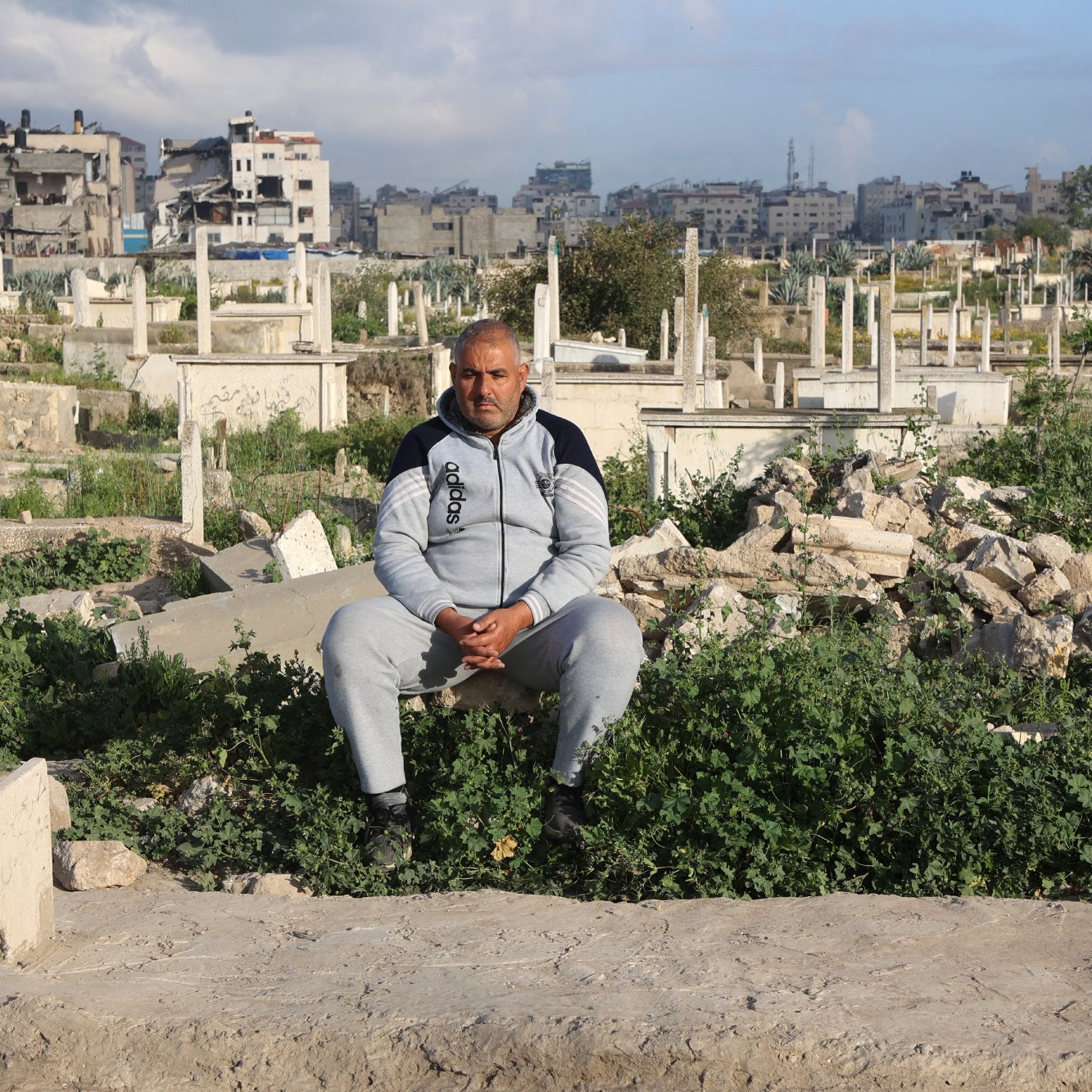 Un uomo seduto in un cimitero, circondato da tombe e vegetazione.