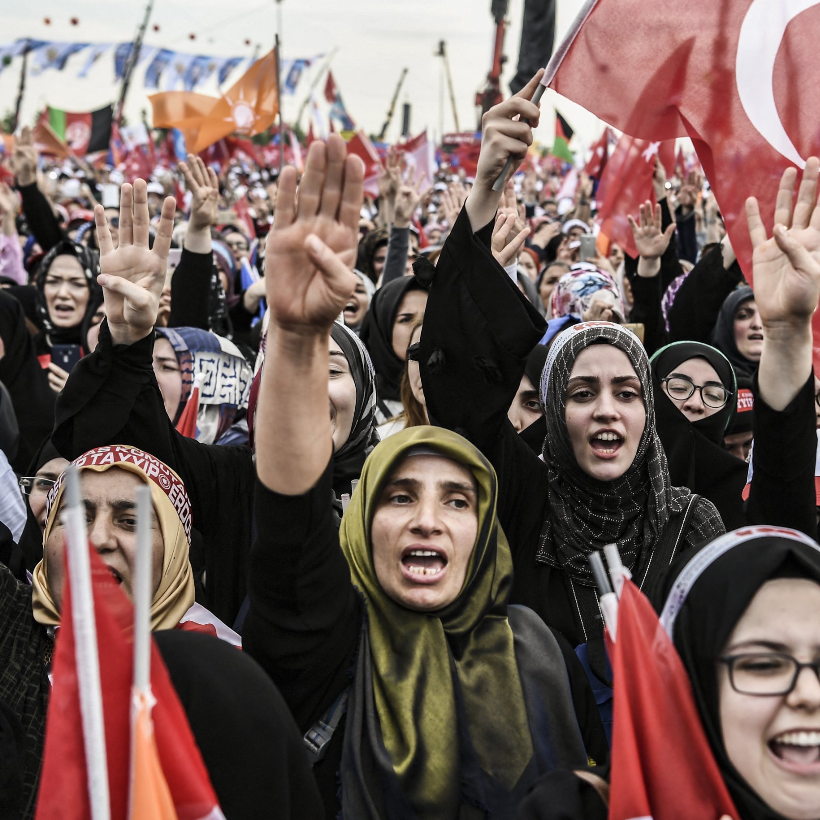 این تصویر نمایی از جمعیتی از زنان را نشان می‌دهد که در یک تجمع یا راهپیمایی شرکت کرده‌اند. آنها پرچم‌های ترکیه را در دست دارند و با شور و هیجان شعار می‌زنند. بیشتر زنان در عکس با حجاب دیده می‌شوند و برخی از آنها با دست علامت پیروزی نشان می‌دهند. فضای عمومی و اجتماعی این تصویر بسیار فعال و پر جنب و جوش به نظر می‌رسد.