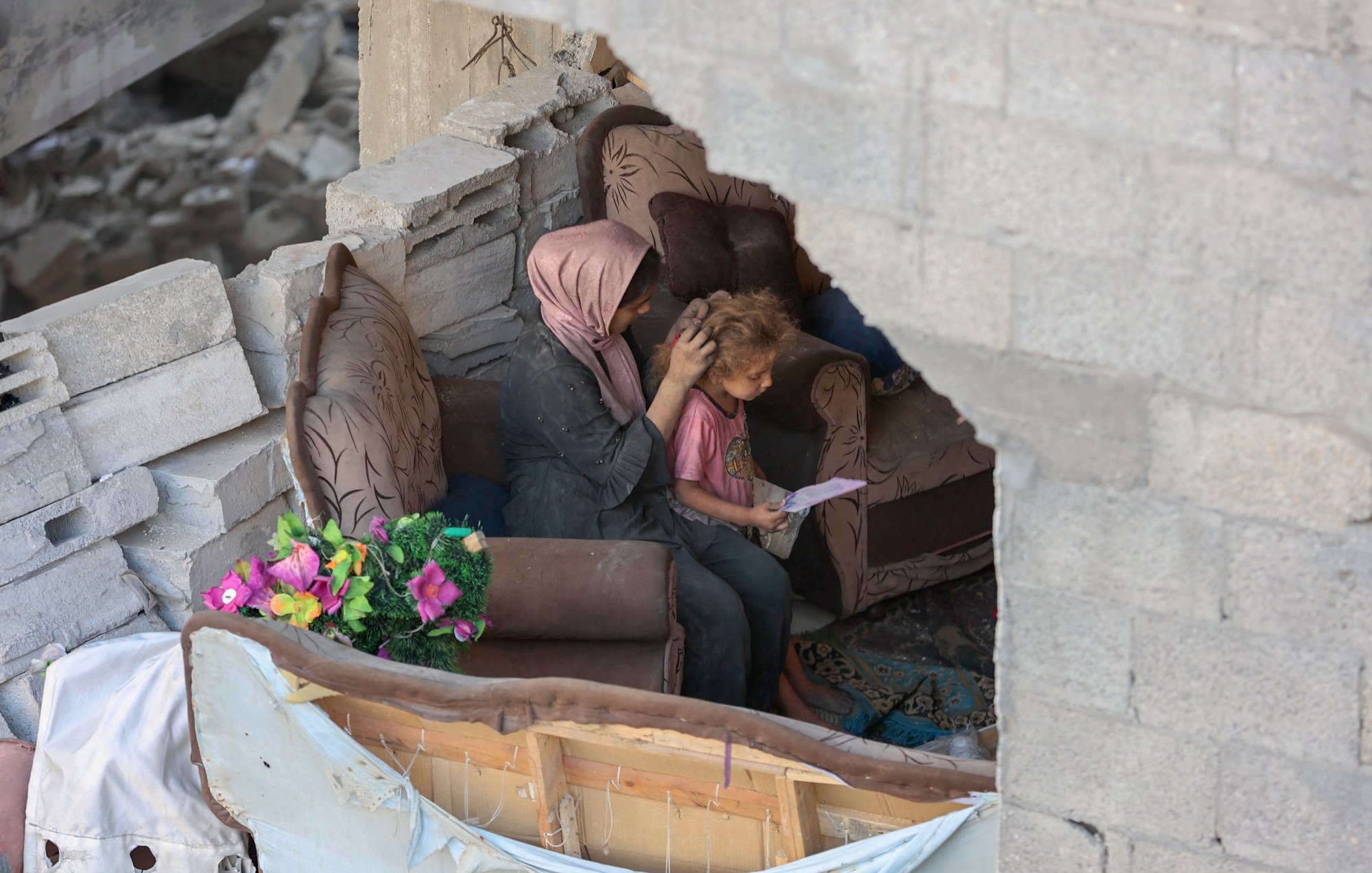 Une mère réconforte son enfant dans un espace endommagé, entourés de débris.