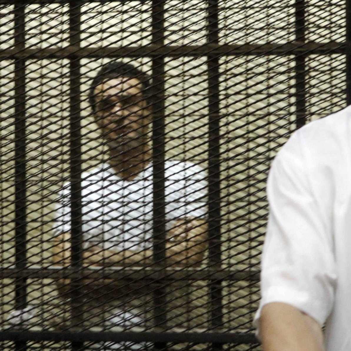 Due uomini in una stanza, uno è dietro una grata di protezione. Atmosfera tesa.