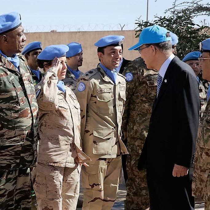 تظهر الصورة مجموعة من الأفراد العسكريين يرتدون بزات الأمم المتحدة الزرقاء، ويبدو أنهم في موقع رسمي. يوجد شخص يحاول التحية، في حين يبدو أن هناك اجتماعًا أو زيارة يقوم بها أحد الشخصيات المهمة. المجموعة تشمل أفرادًا من خلفيات عسكرية متنوعة، ويبدو أن هناك تواصلًا ونقاشًا بينهم. الجو العام يبدو جادًا ومهنيًا، وربما يشير إلى مهمة سلمية.