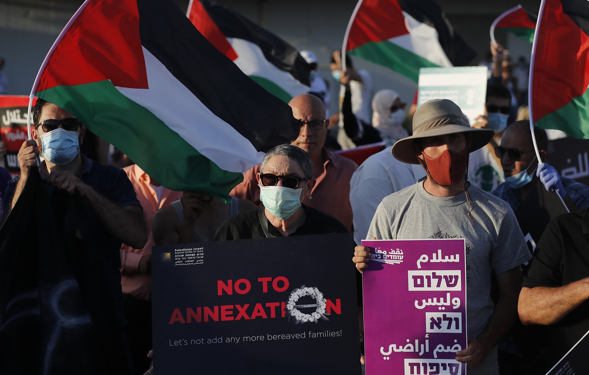 تظهر الصورة مظاهرة حيث يحتشد عدد من الأشخاص Holding لافتات تحمل عبارات تتعلق برفض الضم، بالإضافة إلى العلم الفلسطيني. يرتدي بعض المشاركين كمامات، ويبدو أن المتظاهرين يعبرون عن تضامنهم مع قضايا معينة تتعلق بالفلسطينيين. تُظهر اللافتات عبارات باللغتين العربية والعبرية تعبر عن السلام والتضامن.