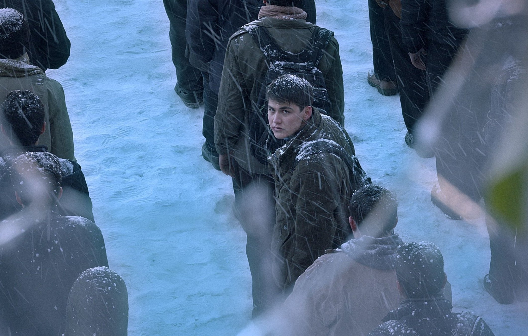 تصویر گروهی از افراد در برف است. یک جوان در مرکز با نگرانی به دور نگاه می‌کند. برف باریده و فضایی سرد است.