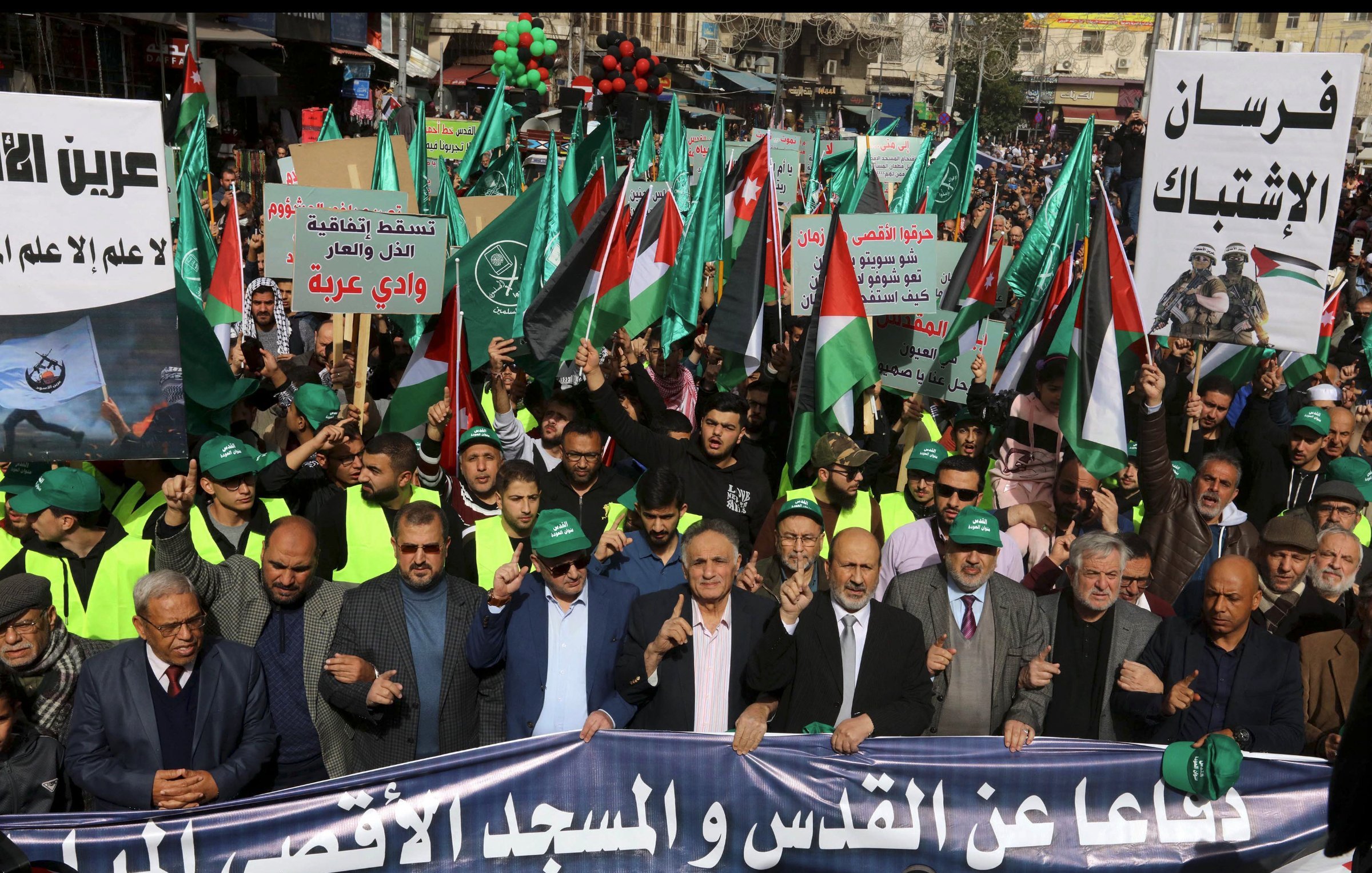 A large crowd marches, holding Palestinian flags and banners, in a show of solidarity.