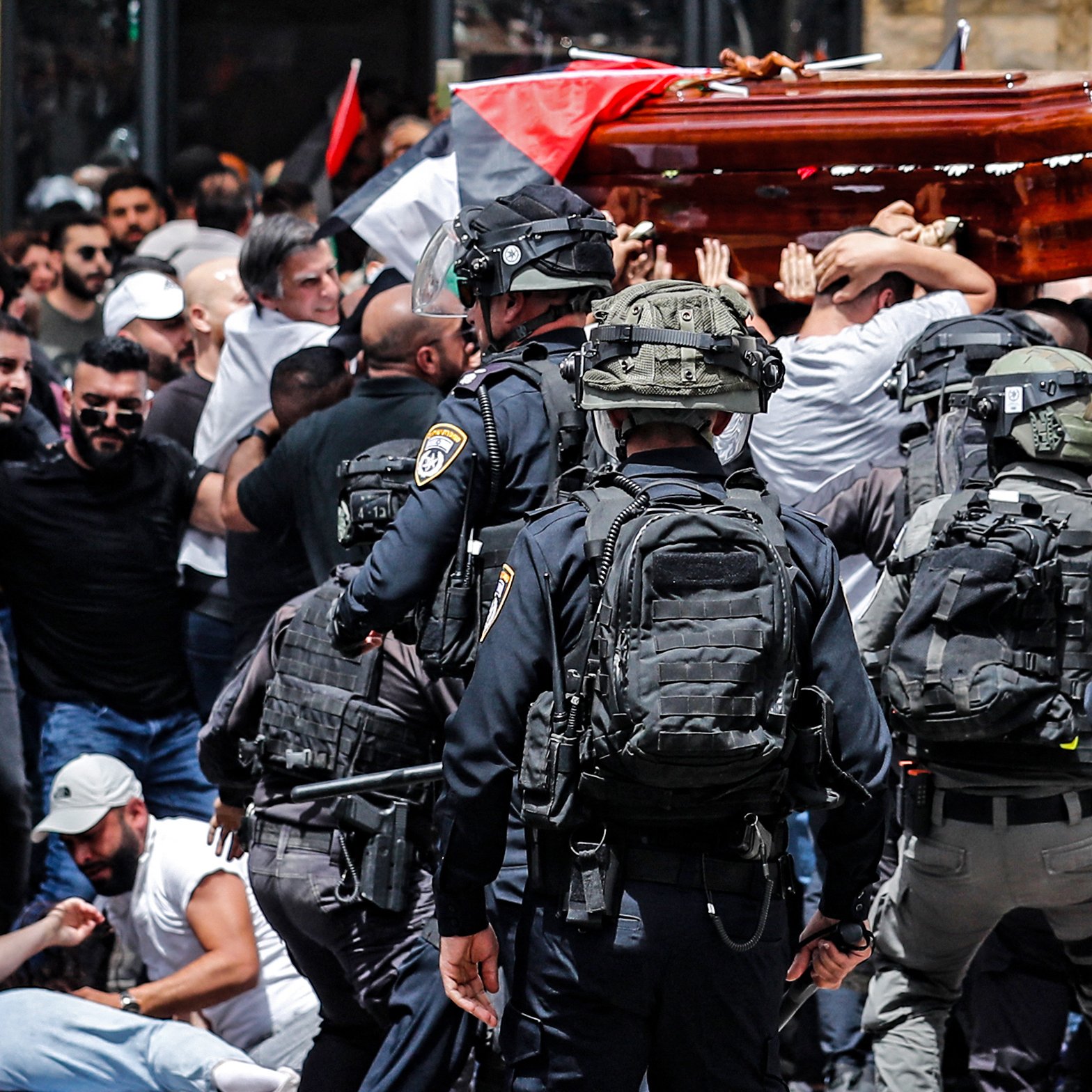 در این تصویر، گروهی از مردم در حال حمل یک تابوت هستند و در اطراف آنها تعدادی نیروی پلیس با تجهیزات نظامی دیده می‌شود. مردم در حال تجمع و اعتراض هستند و پرچم‌هایی را در دست دارند. به نظر می‌رسد این صحنه در یک فضای پرازدحام و تنش‌زای اجتماعی اتفاق می‌افتد. واکنش‌های متفاوتی در چهره‌ها و حرکات افراد مشهود است.
