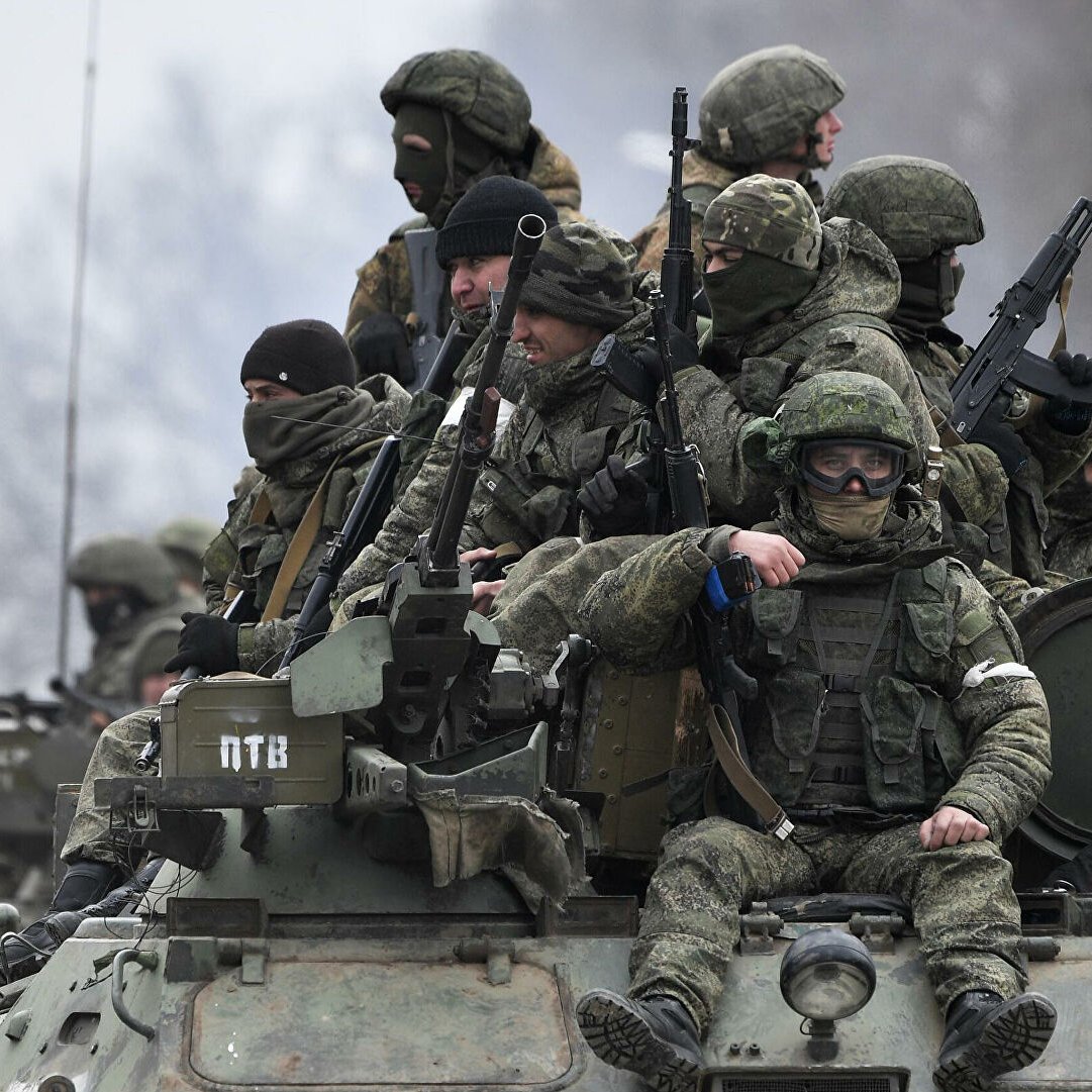 L'immagine mostra un gruppo di soldati equipaggiati con abbigliamento militare e armi, che si trovano su un veicolo blindato. Alcuni di loro indossano maschere o occhiali protettivi, mentre altri appaiono attenti e pronti all'azione. Il contesto è probabilmente un'area di conflitto, con un paesaggio grigio e invernale sullo sfondo. L'atmosfera è seria e tesa, riflettendo la situazione militare.