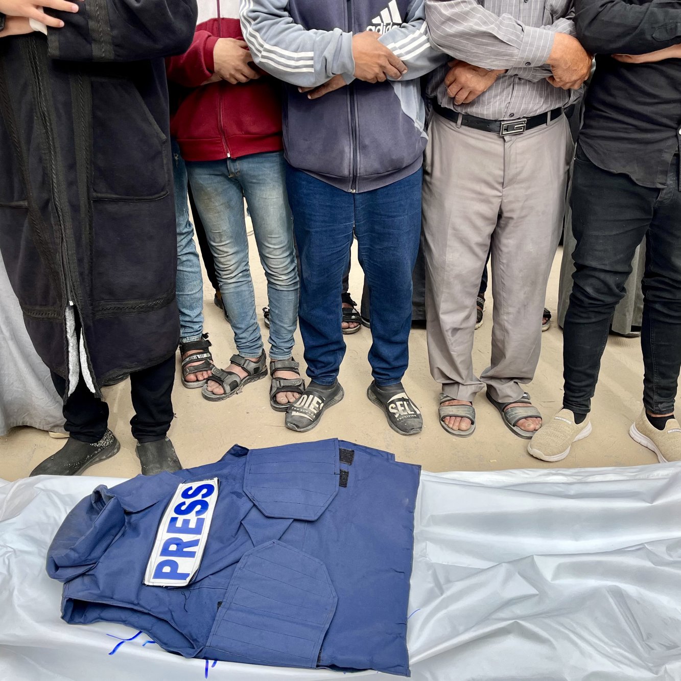 Gruppo di persone in piedi attorno a una giacca con scritto "PRESS" su un telo.