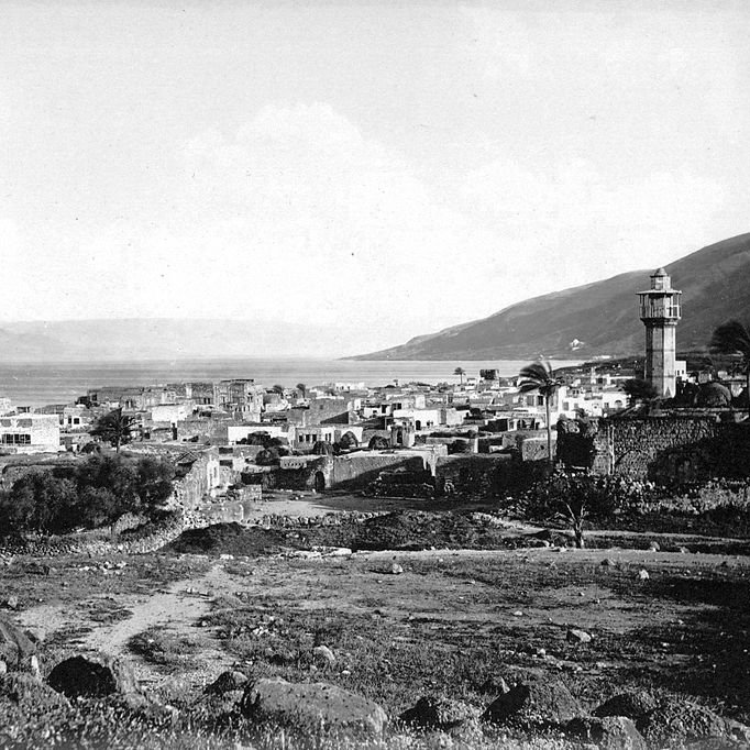 این تصویر نمایش‌دهنده یک مناظر تاریخی از یک روستا یا شهر نزدیک به دریاچه است. در تصویر، یک برج باستانی در سمت راست دیده می‌شود که به واسطه آن، هویت محلی خاصی به چشم می‌آید. ساختمان‌ها در سمت چپ و در پس‌زمینه قرار دارند و برخی از آن‌ها به نظر می‌رسد که با مصالح سنگی ساخته شده‌اند. در دوردست، کوه‌ها و زمین‌های مرتفع قابل مشاهده‌اند و ابرها در آسمان پراکنده‌اند. به طور کلی، این تصویر حس تاریخ و طبیعت آرام را به بیننده منتقل می‌کند.