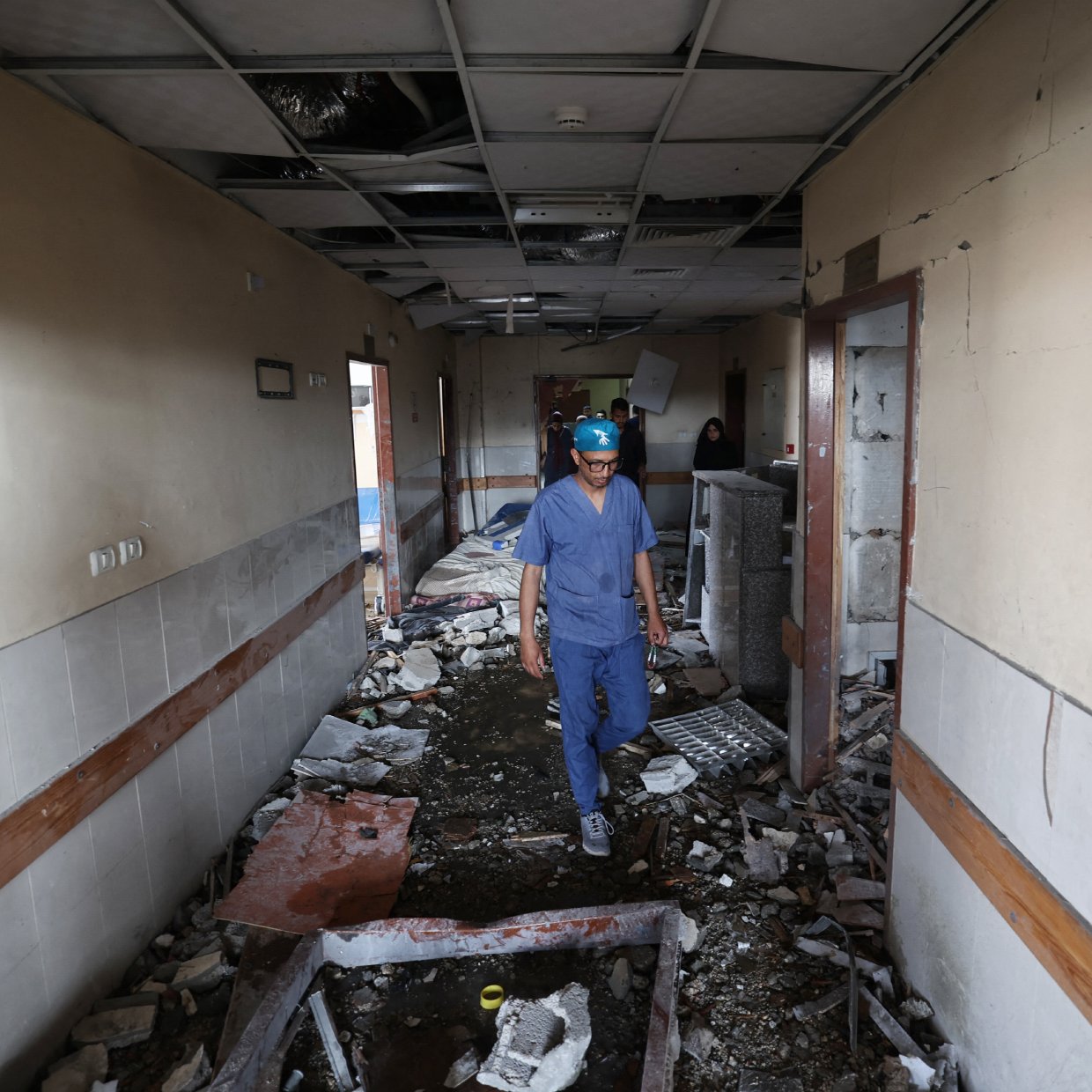 Un uomo in un corridoio distrutto, con macerie e soffitto danneggiato.