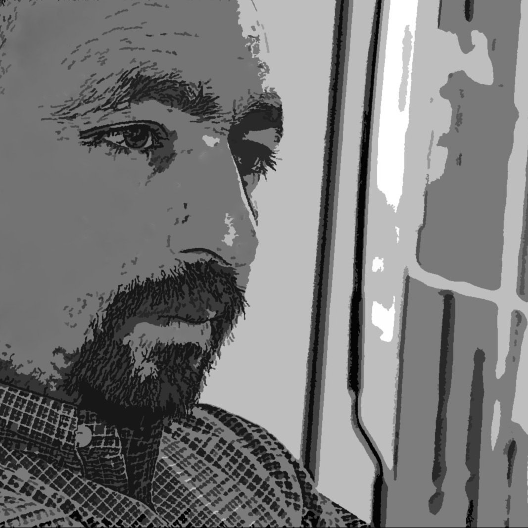 الصورة تظهر رجلًا يبدو في حالة تفكير عميق. ملامحه تُظهر تركيزًا وتأملًا، وهو يرتدي قميصًا مزخرفًا. الإضاءة تنعكس على وجهه، مما يبرز تفاصيله. الخلفية تبدو غير واضحة، مما يعزز من التركيز على العواطف والتعبيرات على وجهه.