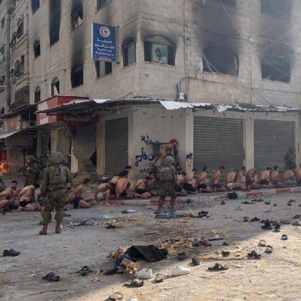 A scene of distress showing people detained in an urban setting with military presence.