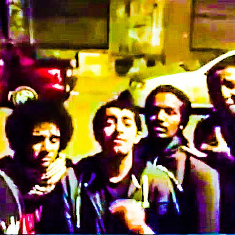 L'image montre un groupe de six personnes posant ensemble devant une voiture garée. Ils semblent être de jeunes adultes, certains portant des lunettes ou ayant des cheveux frisés. L'ambiance est détendue et amicale, et la photo semble avoir été prise de nuit, avec un éclairage un peu faible. La scène donne une impression de camaraderie et de convivialité entre les individus.